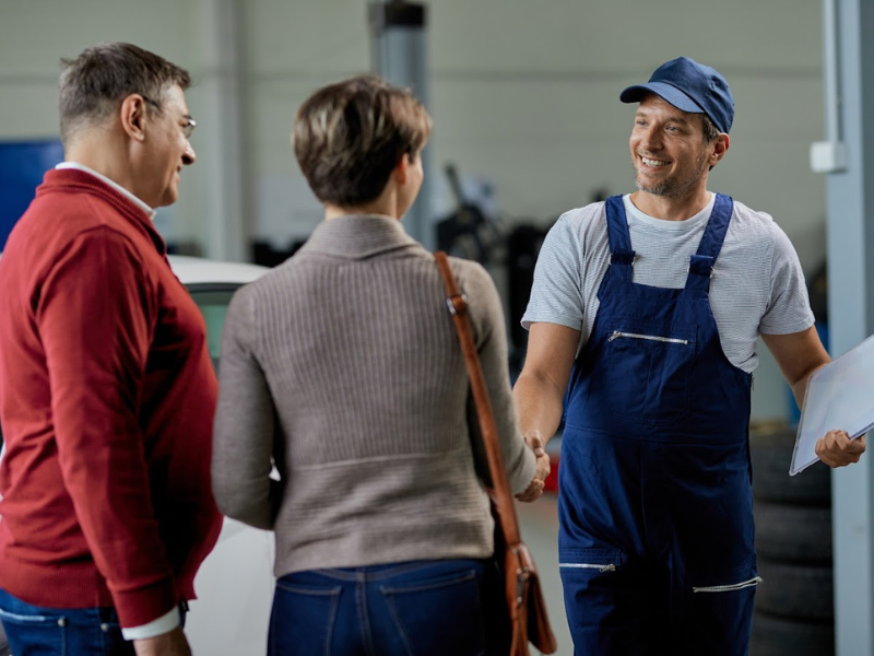 A member of staff at a garage greets customers in front of a white car