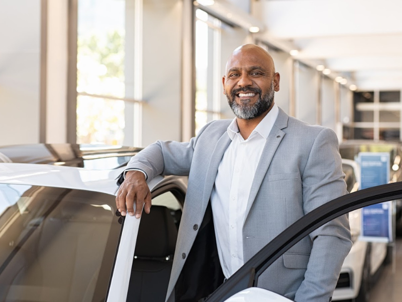 Member of staff in a car dealership stands by a vehicle smiling
